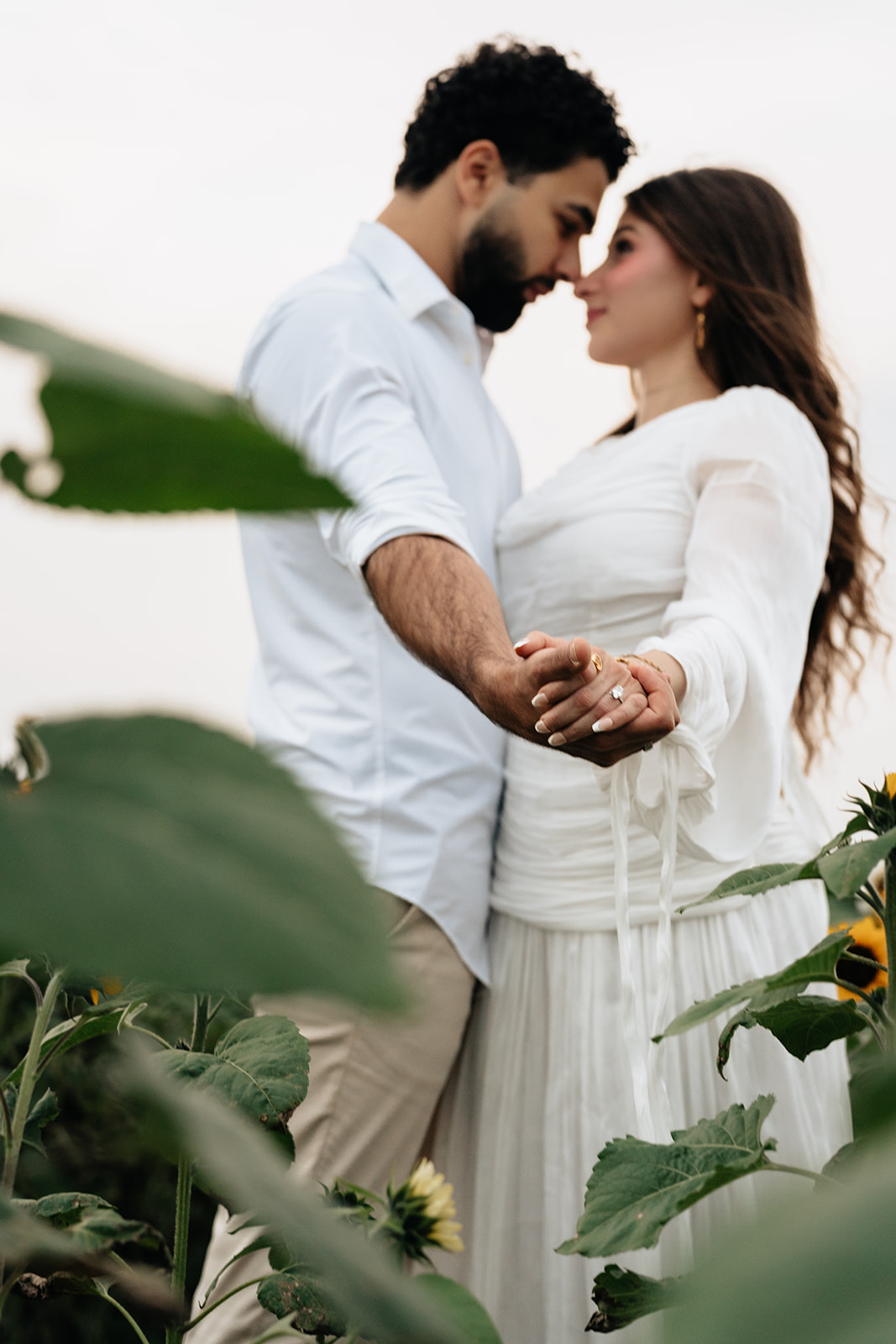 Suemaya and Assad holding hands in a quiet portrait framed by sunflower leaves