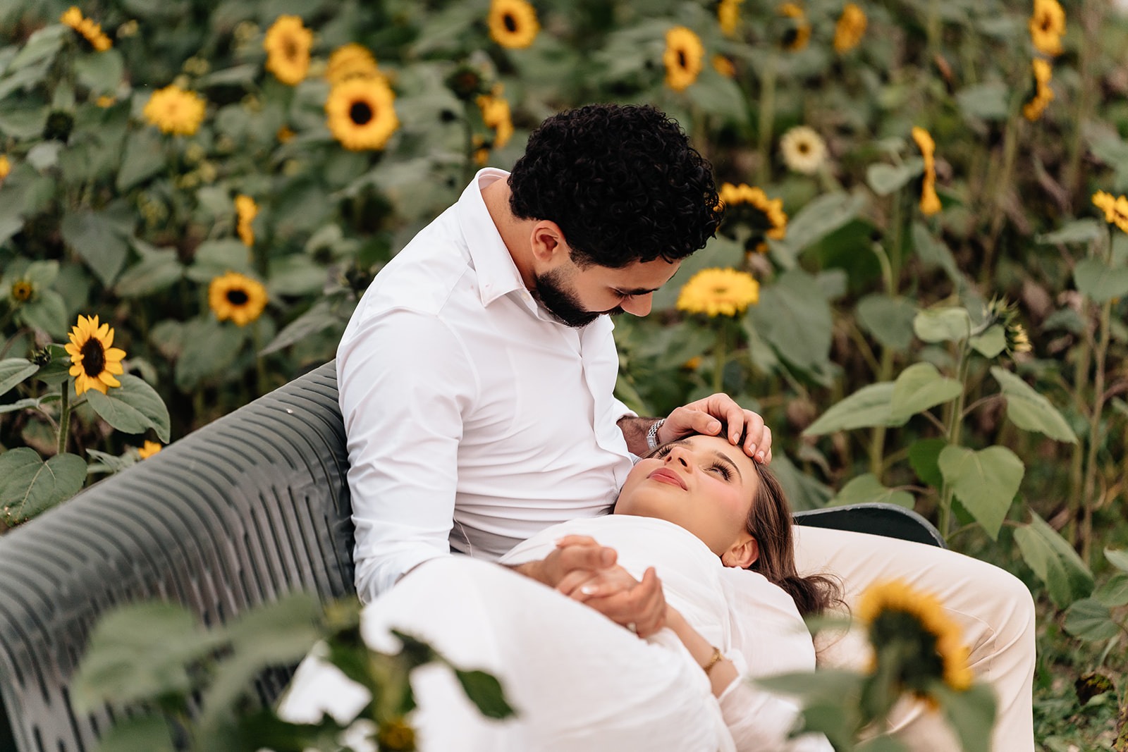 Close portrait of Suemaya and Assad sharing a quiet moment on the bench in the sunflower field