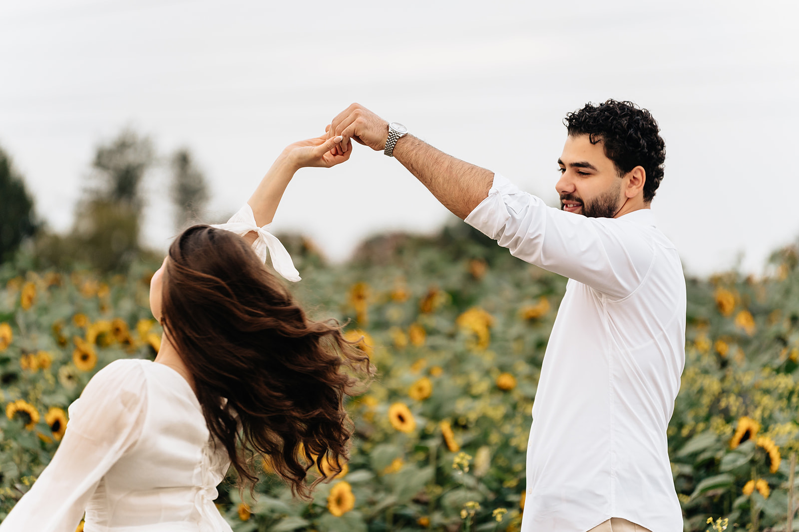Suemaya turning beneath Assad's raised hand at the edge of the sunflower field