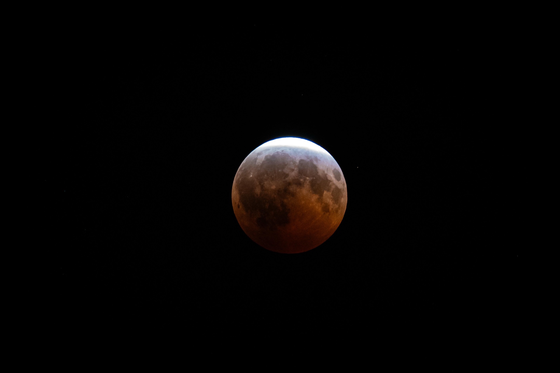 Deep partial lunar eclipse photographed over Northeast Ohio by Rada Abib Photography, the Moon glowing rusty red beneath a bright sunlit sliver